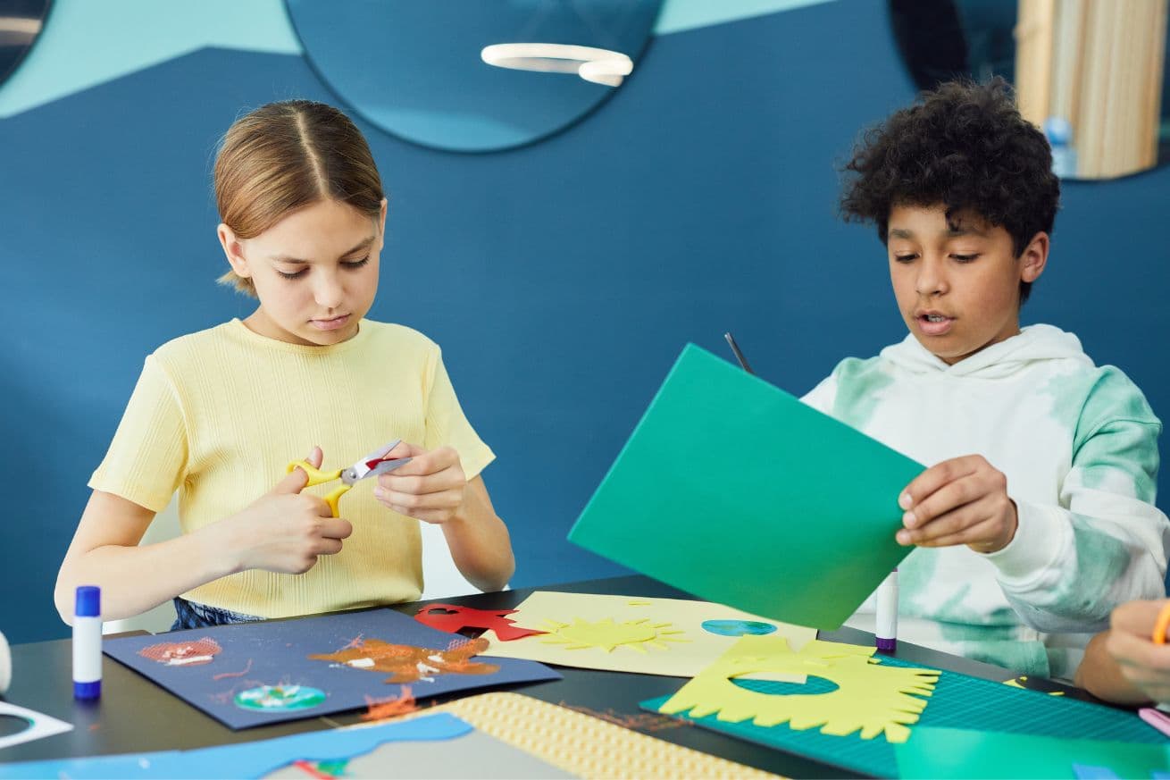 A little girl and little boy are experiencing the physical benefits of art therapy by cutting out shapes with scissors