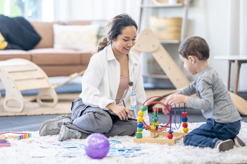 An occupational therapist sitting on the floor playing with blocks with a little boy